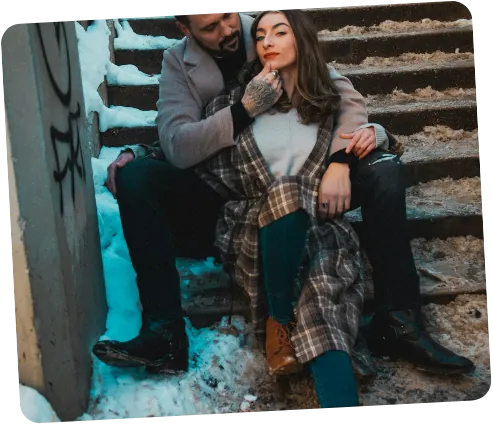 Una coppia seduta su dei gradini innevati, avvolta in un plaid.